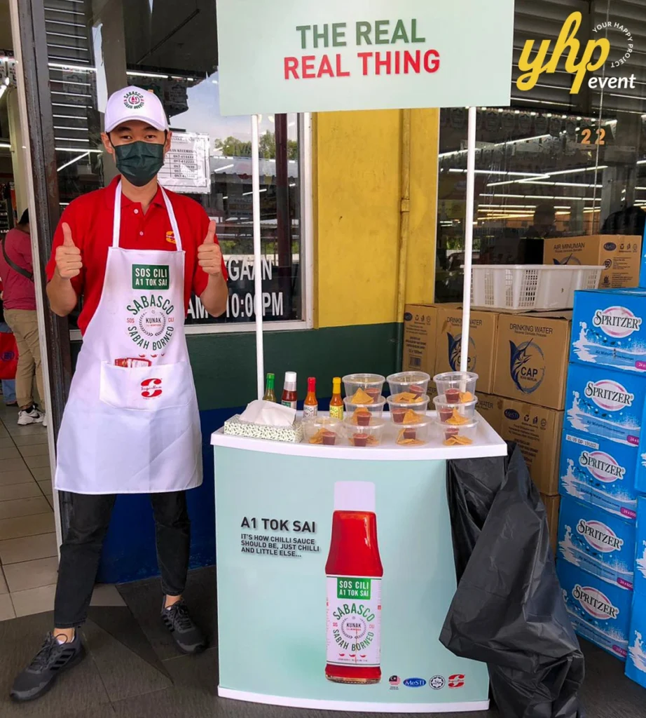 Sabasco A1 Tok Sai East Malaysia Roadshow 4 A man wearing a Sabasco apron giving a thumbs up behind a portable tasting station for Sabah Borneo chili sauce