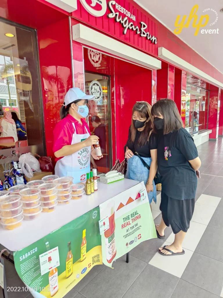 Sabasco A1 Tok Sai East Malaysia Roadshow 5 Staff member at a SugarBun restaurant entrance showing a bottle of Sabasco hot sauce to two interested women