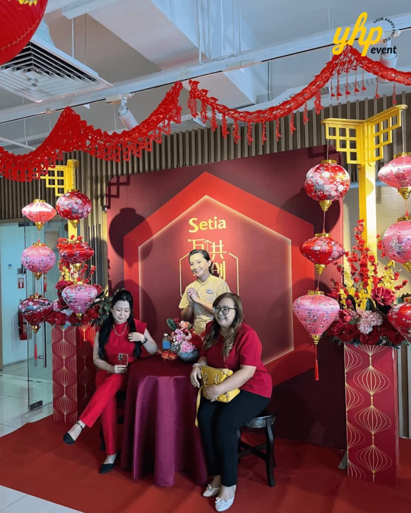 Guests sit at a Chinese New Year photo corner decorated with red lanterns and floral arrangements indoors