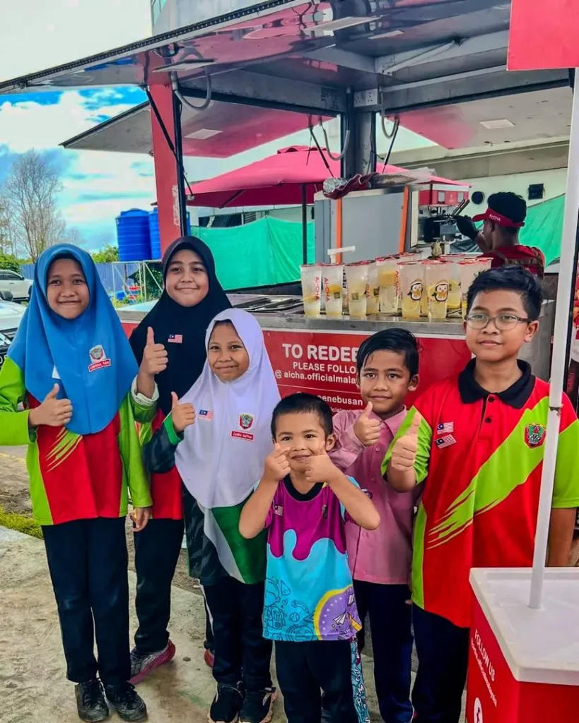 Celebrating Ai Cha’s “Love You 300x” Campaign – Brewing Across Sabah! 10 Children pose happily beside the Ai-CHA redemption booth as cups of iced drinks sit ready for collection