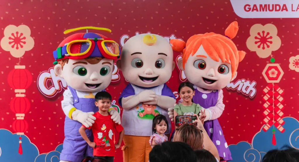 Children posing for a photo with CoComelon mascots JJ, Cody, and Nina on a red festive backdrop in Kota Kinabalu 