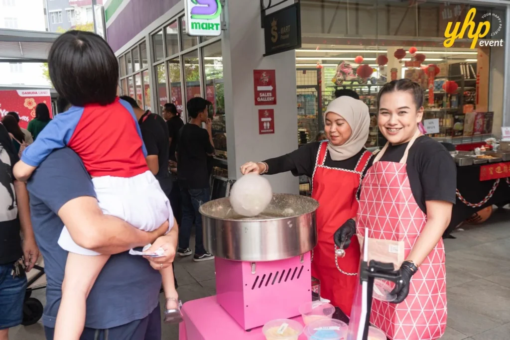 Event staff making fresh cotton candy for a young child and parent at a CoComelon themed celebration