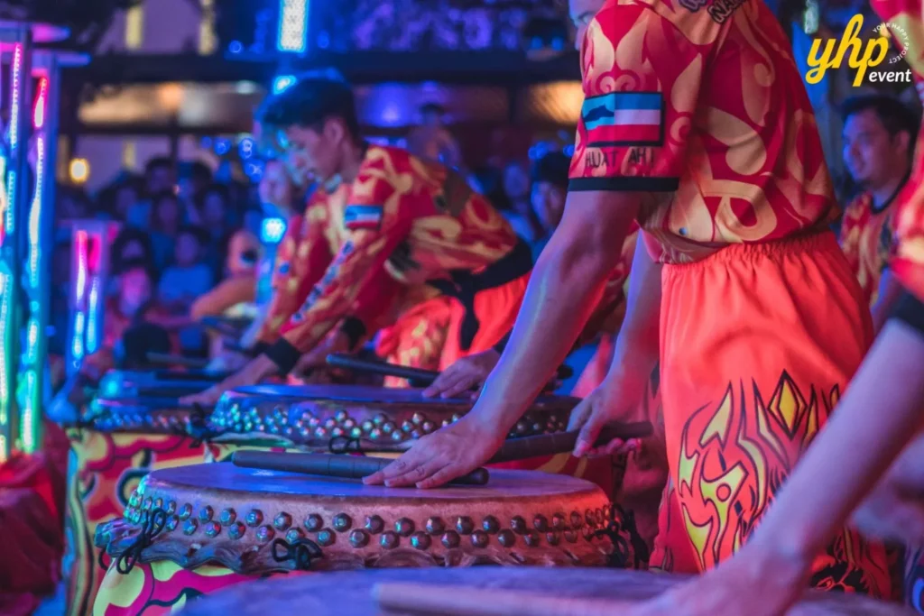 Performers in red and gold uniforms playing traditional Chinese drums at a loud, festive celebration