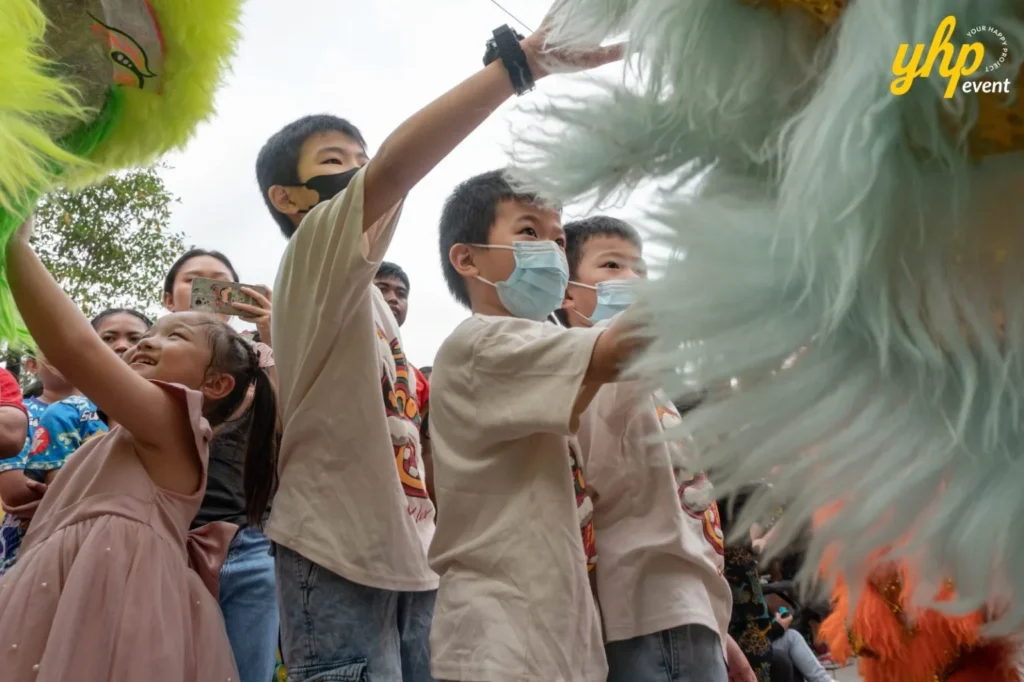Children reaching out to touch a colorful lion dance costume during a community cultural festival