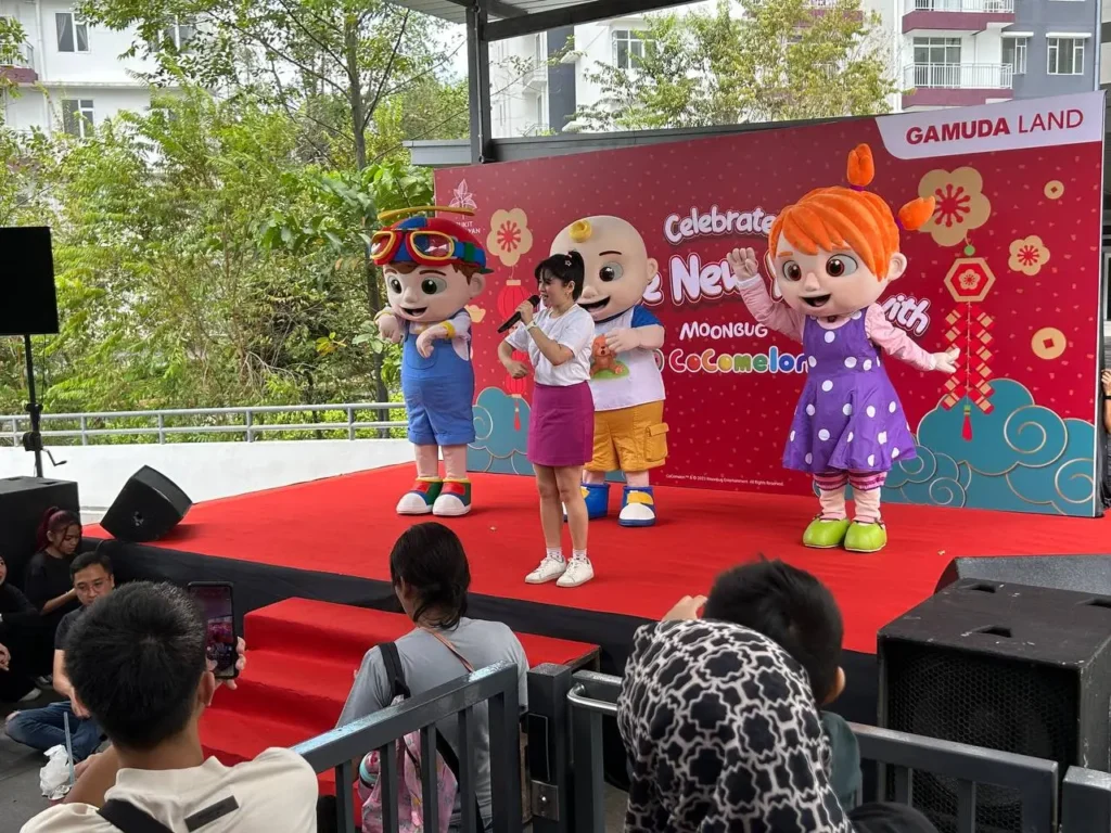 Children and parents from all over kk watching a CoComelon stage performance featuring JJ and Cody mascots dancing