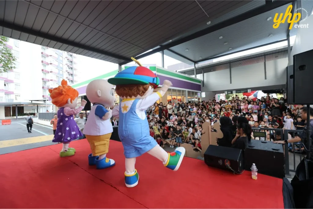 CoComelon mascots JJ, Cody, and Nina dancing on stage in front of a large crowd of families and kids