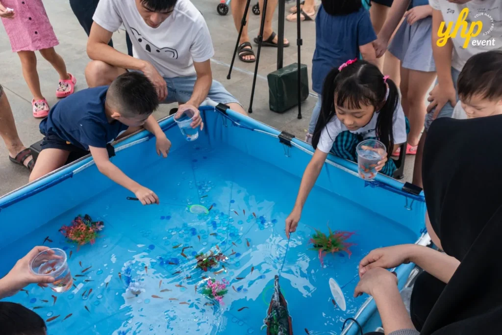 Kids using small nets to catch goldfish in a blue portable pool during a CoComelon themed fun fair