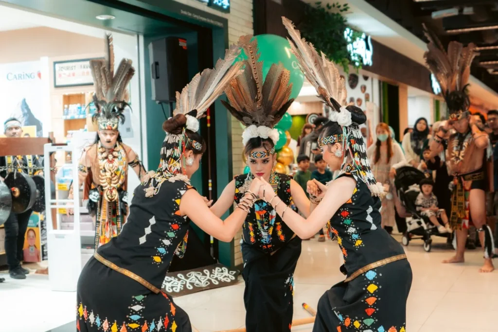 Embrace the Essence of Caring Pharmacy #Promosi Tadau Kaamatan 12 Female cultural dancers in traditional black embroidered Kadazan costumes performing at Caring Pharmacy