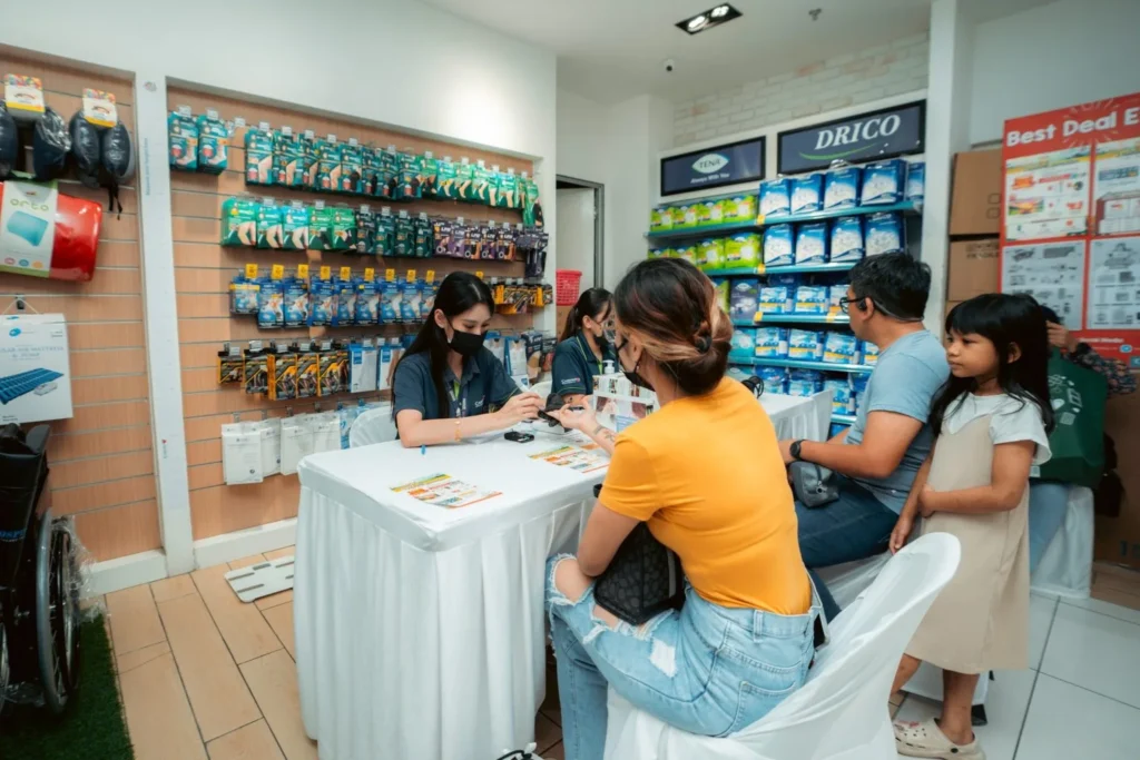 Embrace the Essence of Caring Pharmacy #Promosi Tadau Kaamatan 14 Caring Pharmacy staff providing personal health consultations to a family at a retail service booth