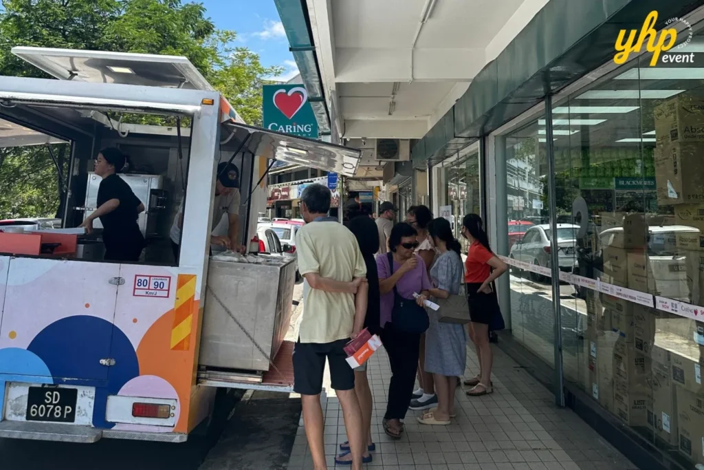 Embrace the Essence of Caring Pharmacy #Promosi Tadau Kaamatan 17 A mobile food truck parked outside a Caring Pharmacy storefront with a queue of customers waiting