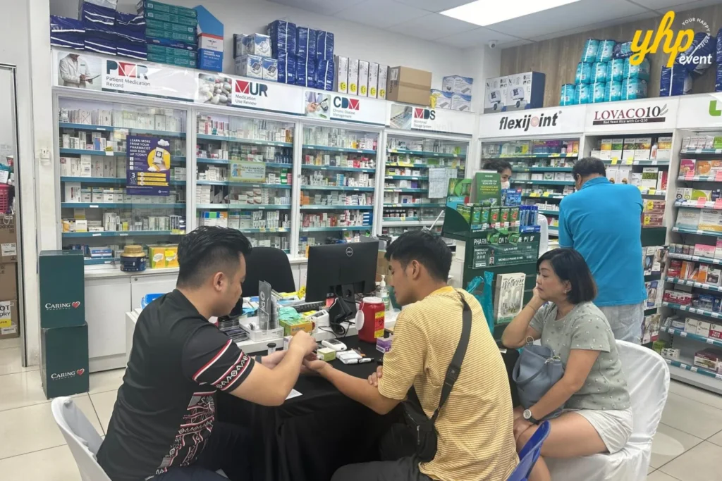 Embrace the Essence of Caring Pharmacy #Promosi Tadau Kaamatan 18 A male customer receiving a health check from a pharmacist at a dedicated Caring Pharmacy service desk