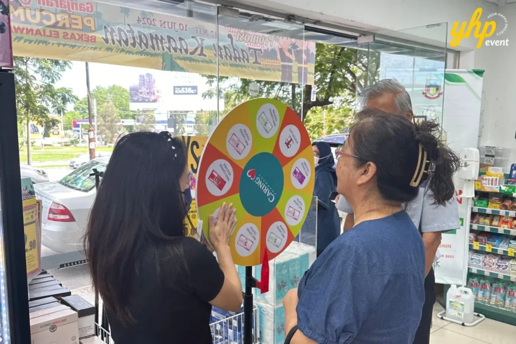 Embrace the Essence of Caring Pharmacy #Promosi Tadau Kaamatan 19 A customer spinning a colorful prize wheel to win vouchers and gifts at a Caring Pharmacy promotion