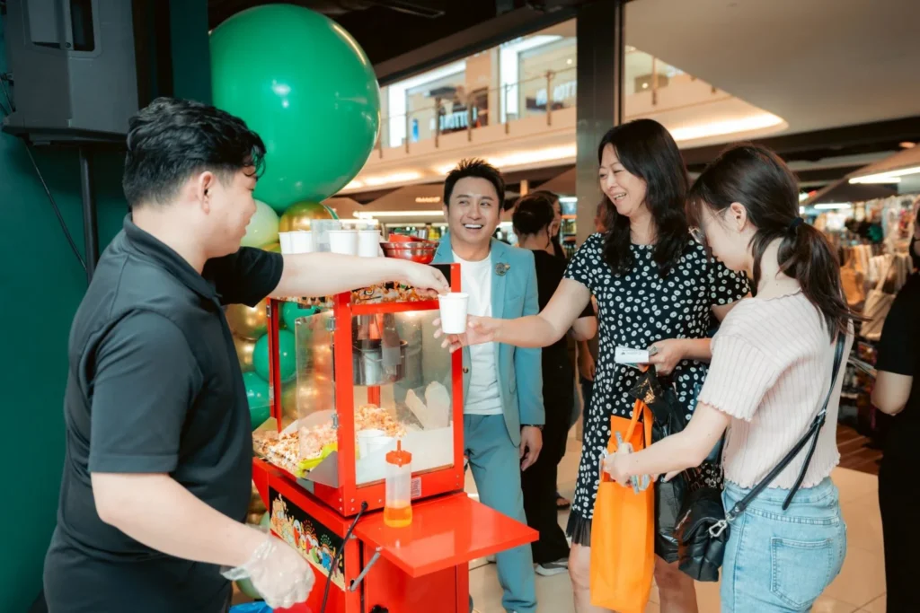 Embrace the Essence of Caring Pharmacy #Promosi Tadau Kaamatan 4 Caring Pharmacy event staff serving fresh popcorn to customers at a store promotion