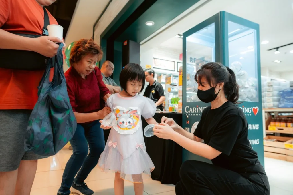 Embrace the Essence of Caring Pharmacy #Promosi Tadau Kaamatan 7 A young child and her family receiving a prize capsule from a Caring Pharmacy staff member