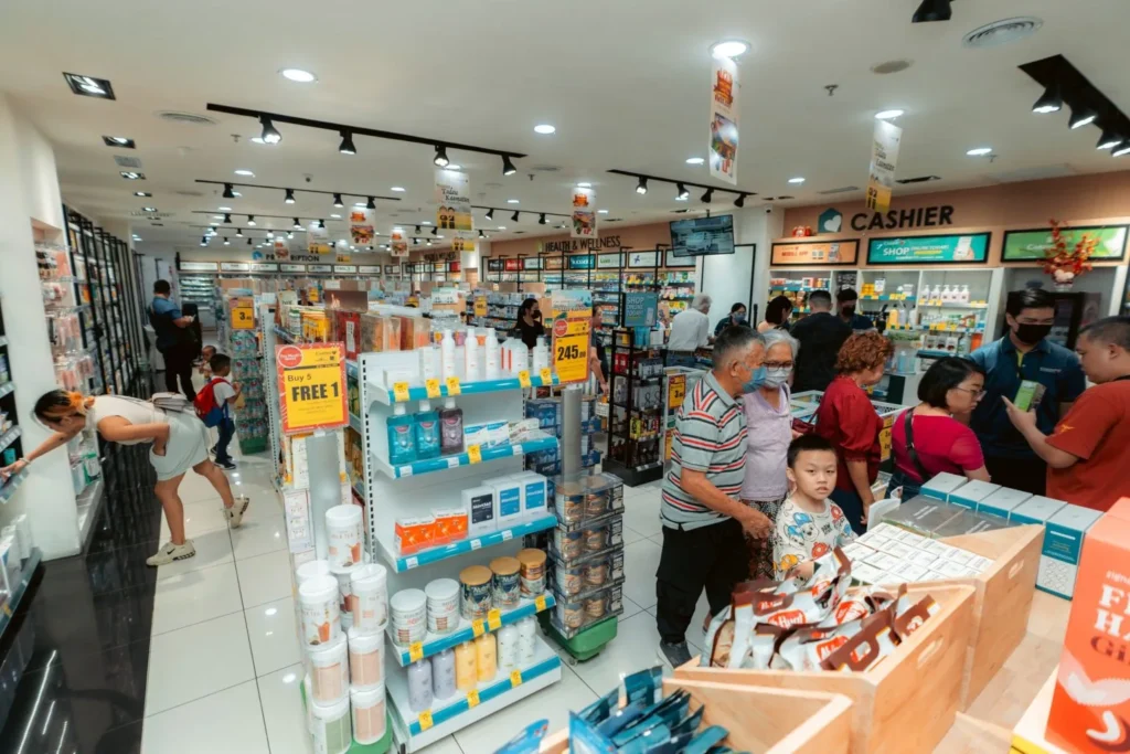 Embrace the Essence of Caring Pharmacy #Promosi Tadau Kaamatan 8 Wide view of shoppers browsing well-stocked shelves and health products inside a bright Caring Pharmacy branch