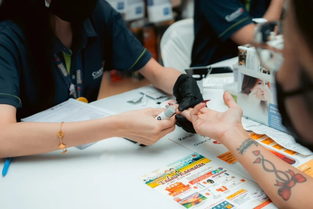 Embrace the Essence of Caring Pharmacy #Promosi Tadau Kaamatan 10 Close-up of a Caring Pharmacy professional performing a finger-prick blood glucose test for a store customer