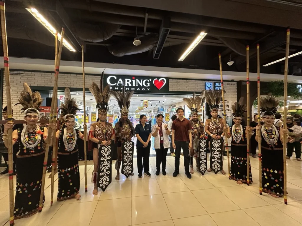 Caring Pharmacy Kaamatan & Gawai Campaign Launch 2 Sabah Traditional performers in feathered attire stand with bamboo poles outside Caring Pharmacy Imago Mall