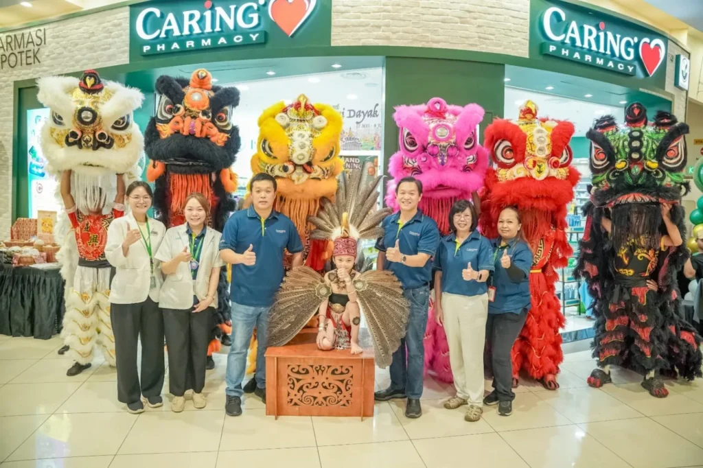 Caring Pharmacy Kaamatan & Gawai Campaign Launch 11 Caring Pharmacy AEON Mall Kuching team poses with lion dance costumes and a child in traditional attire at the storefront