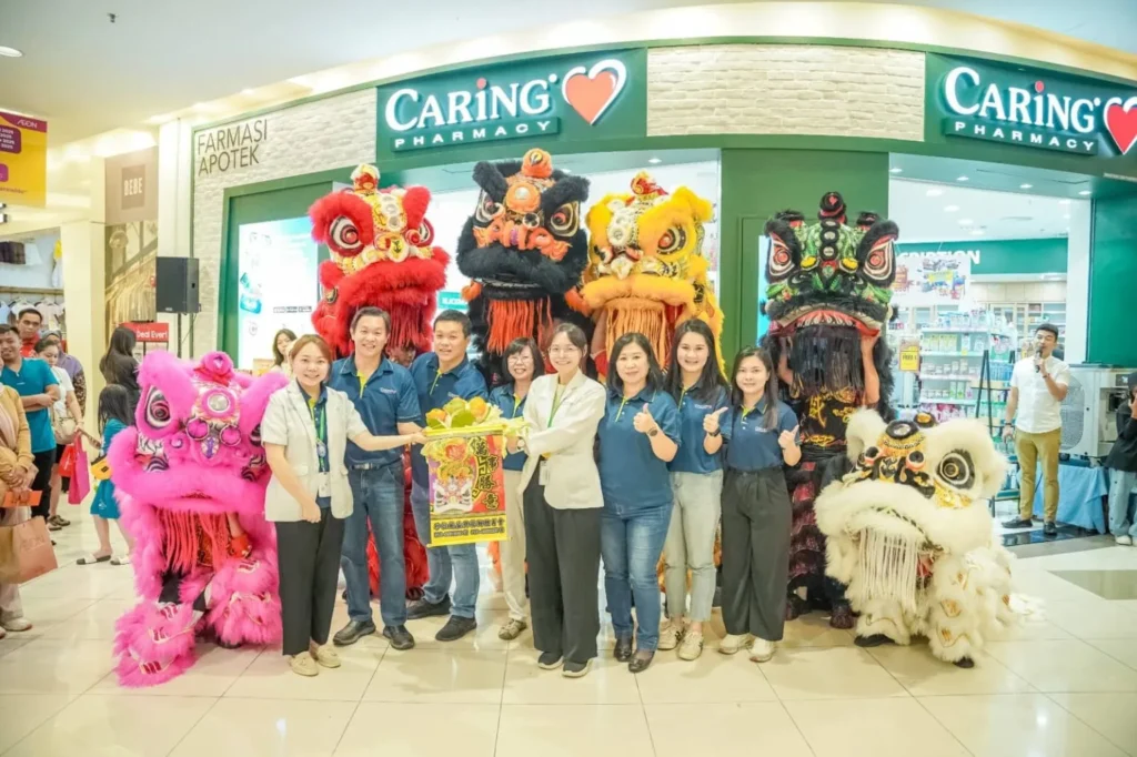 Caring Pharmacy Kaamatan & Gawai Campaign Launch 5 Caring Pharmacy Kuching employees pose with lion dance troupes outside the storefront