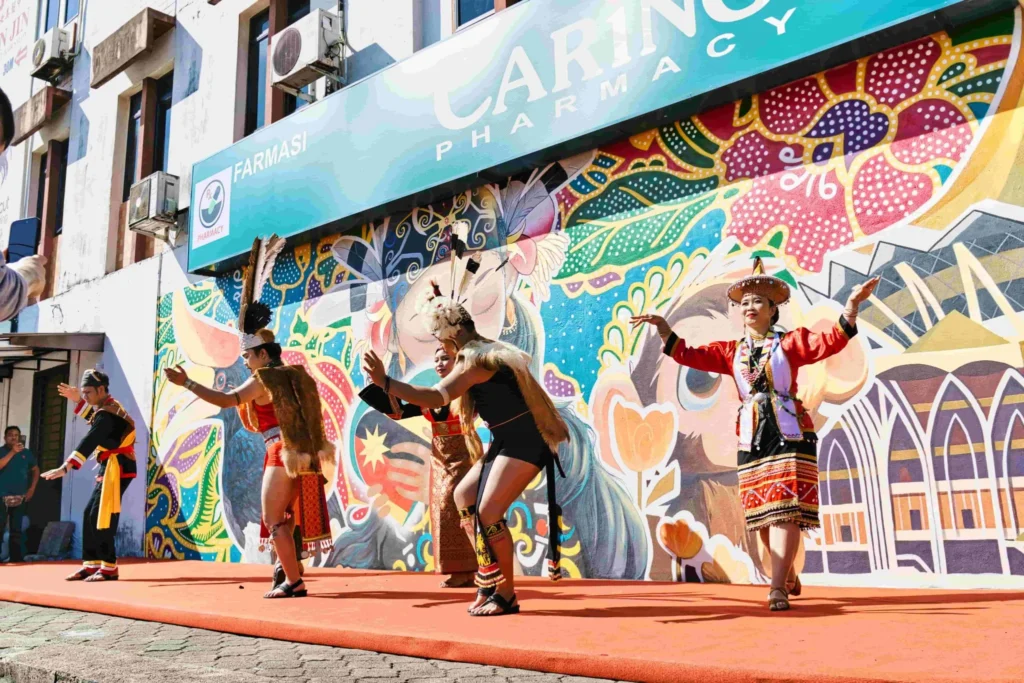 Traditional dancers perform in front of the Caring Pharmacy mural during an outdoor cultural showcase