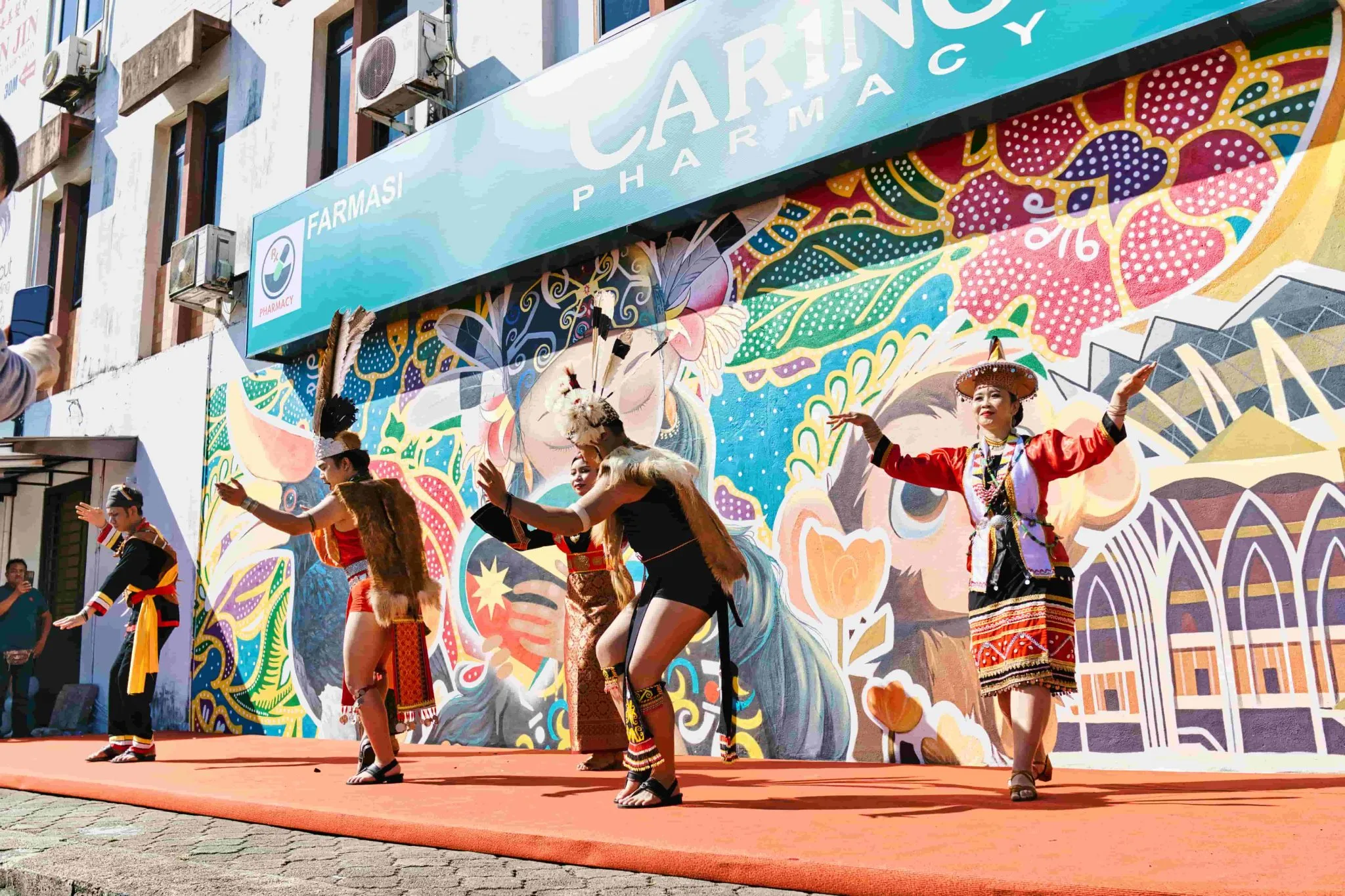 Caring Pharmacy Mural Unveiling l Kota Sentosa Kuching 1 Traditional dancers perform in front of the Caring Pharmacy mural during an outdoor cultural showcase