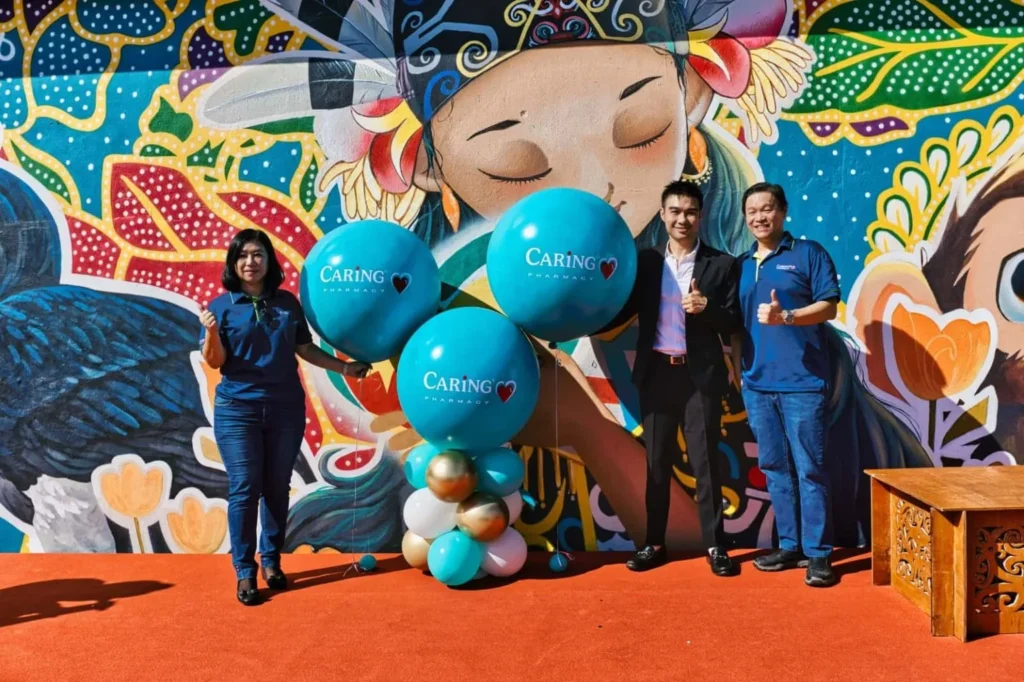Caring Pharmacy Mural Unveiling l Kota Sentosa Kuching 4 Staff members stand by branded balloons in front of the Caring Pharmacy Kota Sentosa Kuching mural during the opening event