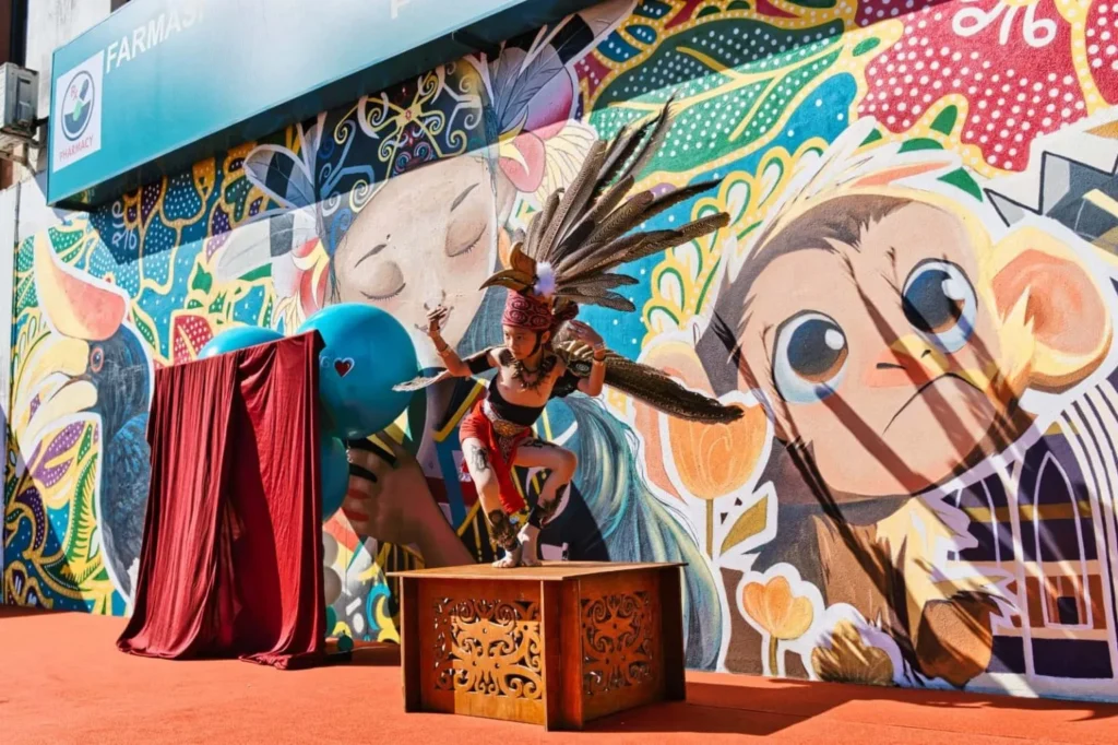 Caring Pharmacy Mural Unveiling l Kota Sentosa Kuching 5 Young Sarawakian cultural performer in feathered costume poses on a platform before the Caring Pharmacy mural backdrop