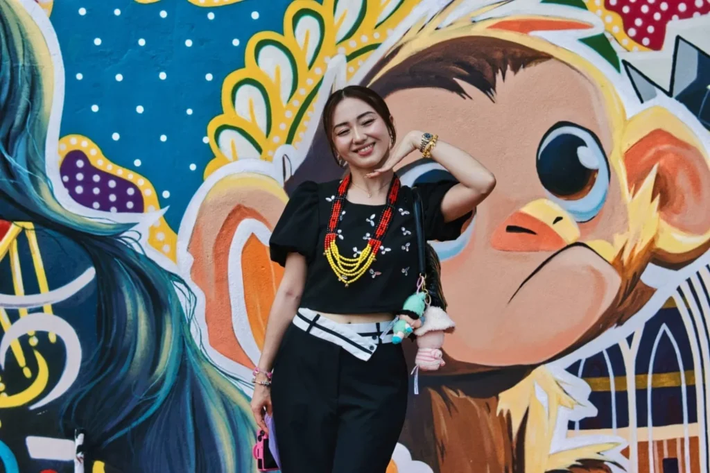 Caring Pharmacy Mural Unveiling l Kota Sentosa Kuching 7 Woman poses in front of a colorful monkey mural beside Caring Pharmacy during the outdoor cultural event