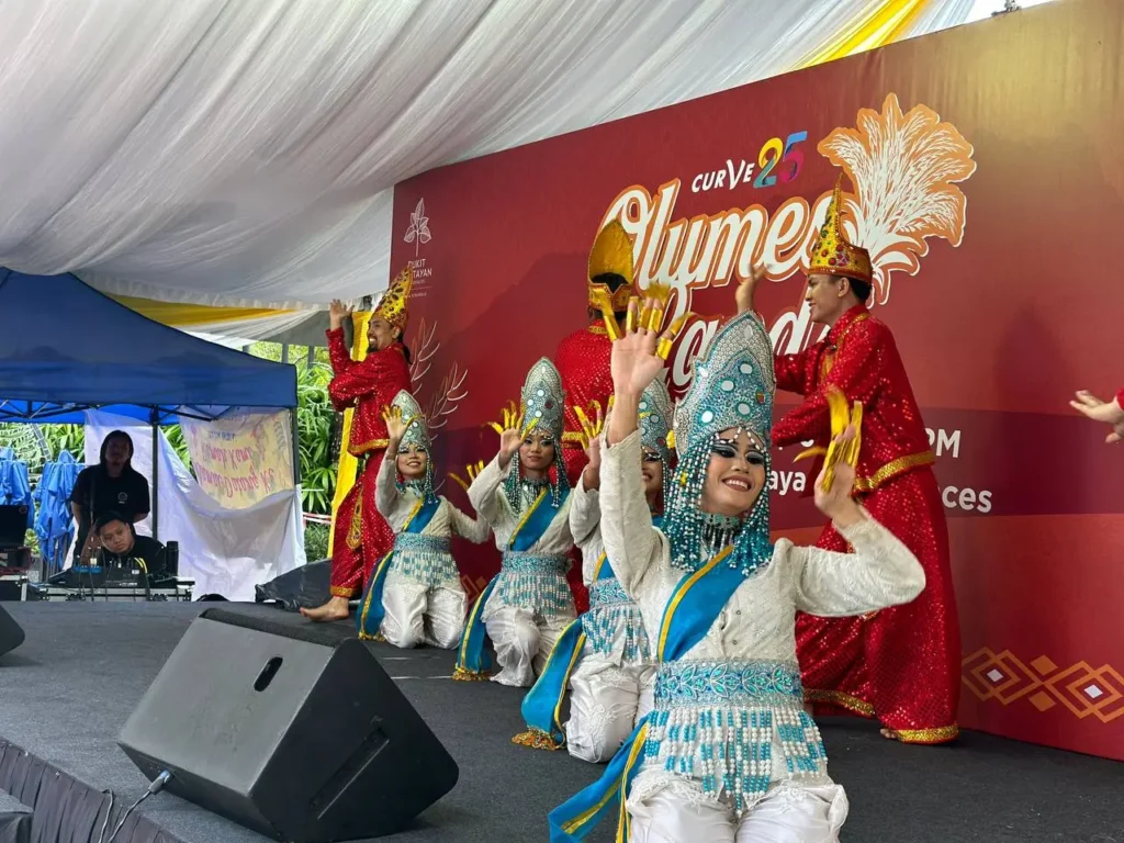Curve25 Olumes Land : Kaamatan Celebration in Kota Kinabalu 2 Traditional Malaysian dancers in ornate silver and red costumes perform on stage at a Bukit Bantayan event