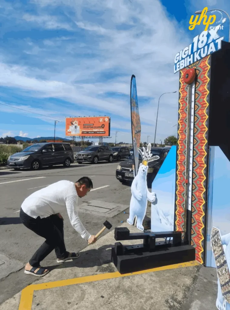 Fresh & White Borneo Edition: Out-of-Home Activation Across Sabah & Sarawak 6 Man plays high striker game near outdoor promotion stand with mountain billboard and blue sky background
