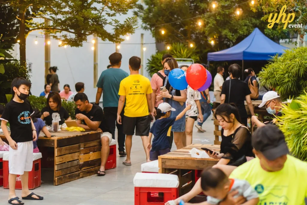 Celebrating the Grand Launch of Curve25 21 Families enjoy an outdoor community festival with rustic pallet seating, string lights, and colorful balloons