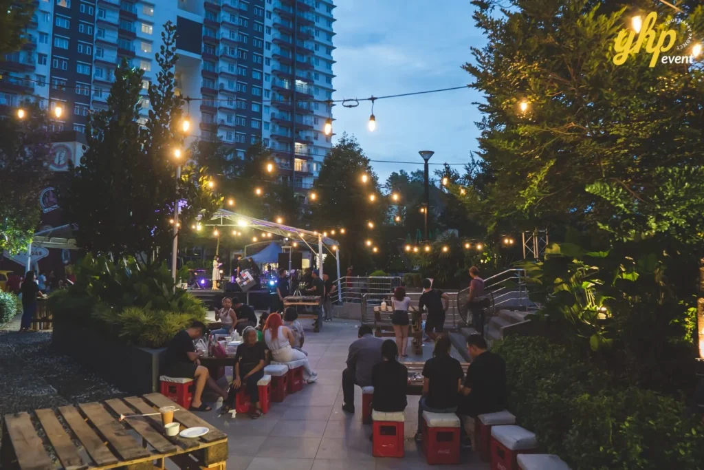 Celebrating the Grand Launch of Curve25 22 Evening outdoor event featuring live music under a canopy with festive string lights and people on red crate seats