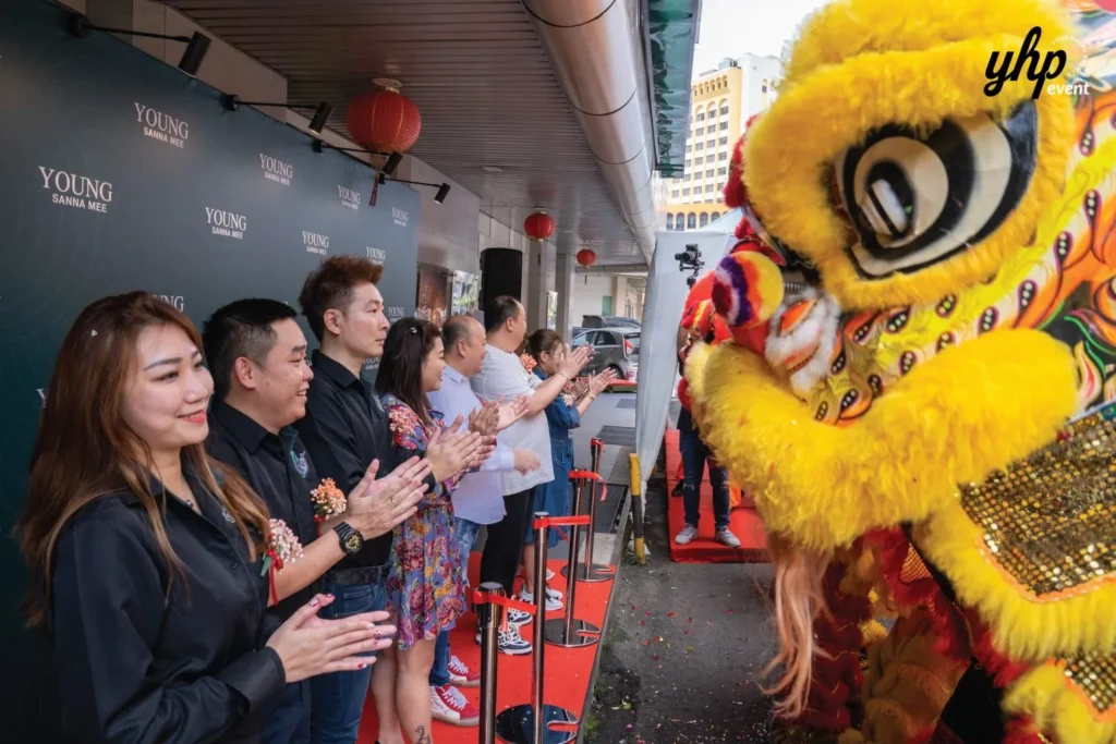 Grand Opening of Young Sanna Mee in Sabah - Enjoy Delicious and Healthy Noodles 11 Guests clapping as they face a vibrant yellow lion dance character at the Young Sanna Mee opening event