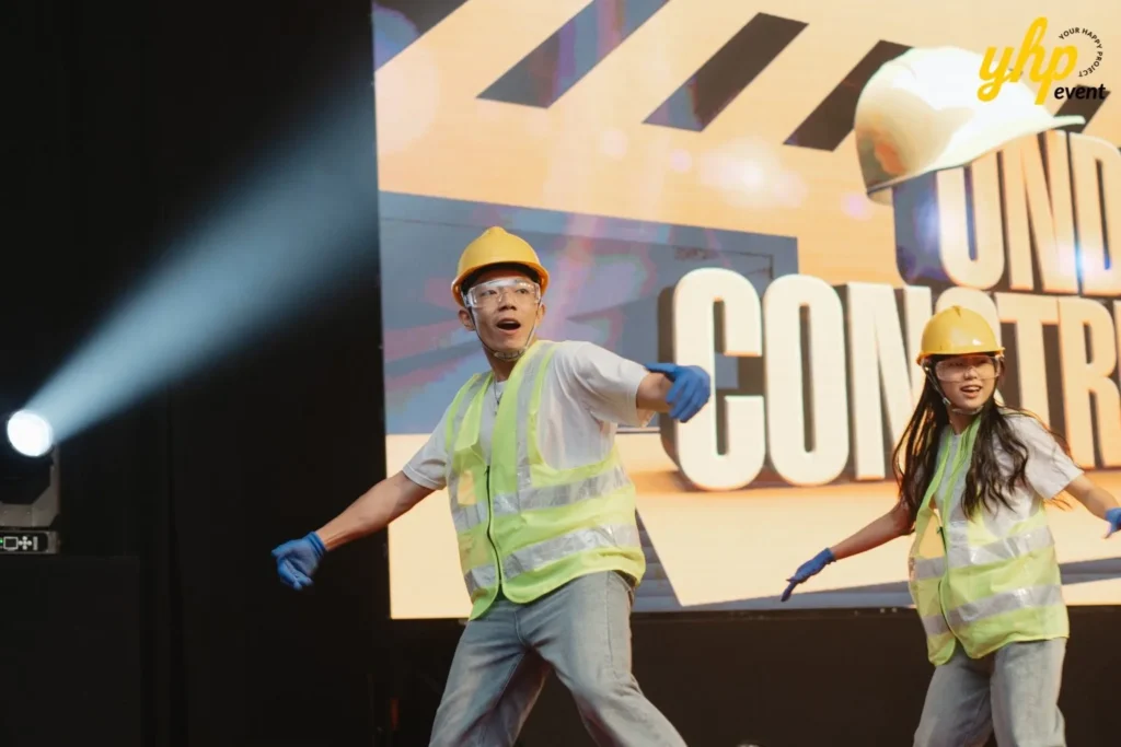 Performers wearing yellow hard hats and safety vests dancing