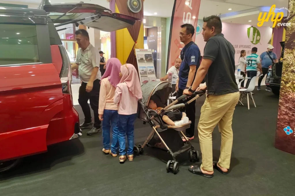 Experience Innovation and Comfort at the Nissan Roadshow 4 Family with a stroller looking at the open trunk of a red Nissan Serena van at a mall car showcase