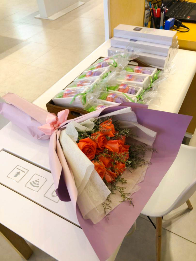 A bouquet of orange roses and small gift boxes arranged on a white table inside a modern mobile phone retail store