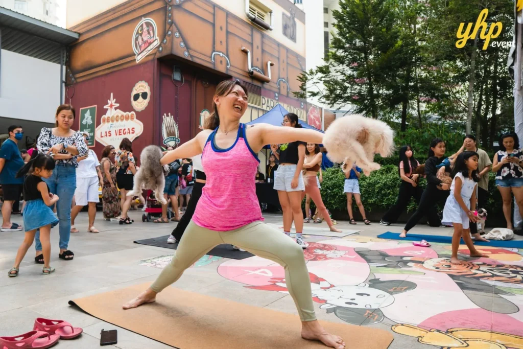 Smiling woman holding two small dogs while performing a warrior yoga pose