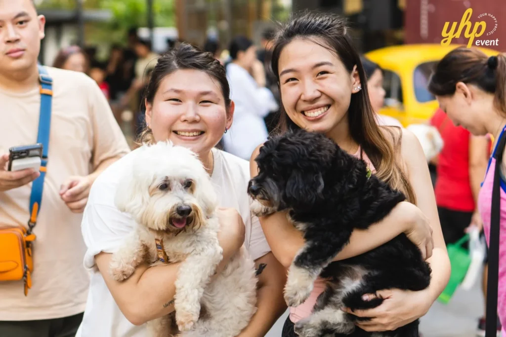 Two women smiling while holding a white maltese and a black poodle dog