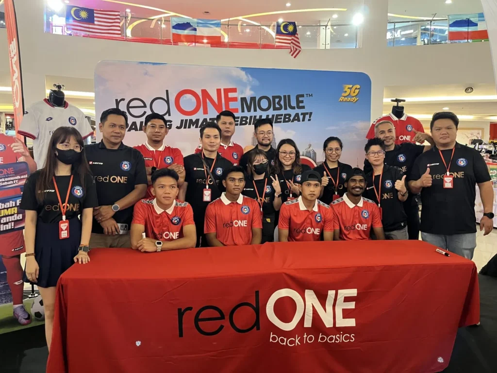 REDone Roadshow: Meet & Greet with Sabah FC (Football Club) 5 Group photo of redONE Mobile staff and Sabah football club players behind a branded red table at a marketing event