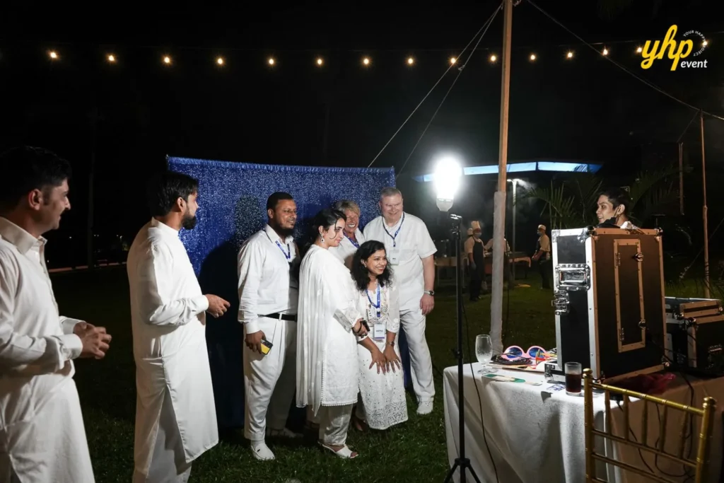 YHP Event- Instant Photobooth Group of guests in white attire posing at a photo booth with a blue backdrop