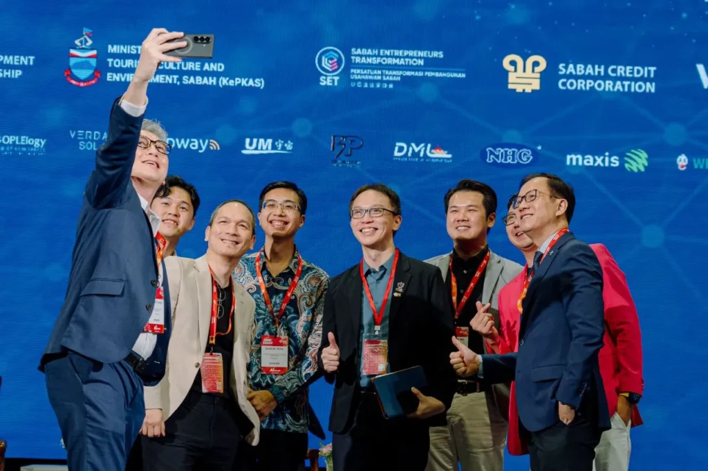SME Expo AI Summit 2025 - Sabah International Convention Centre (SICC) 6 Attendees pose for a selfie at AI Summit 2025 beneath partner logos during event networking