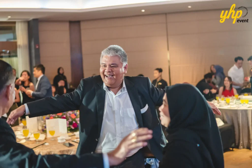 Smiling man in a suit greeting guests with open arms at a lively corporate gala dinner celebration
