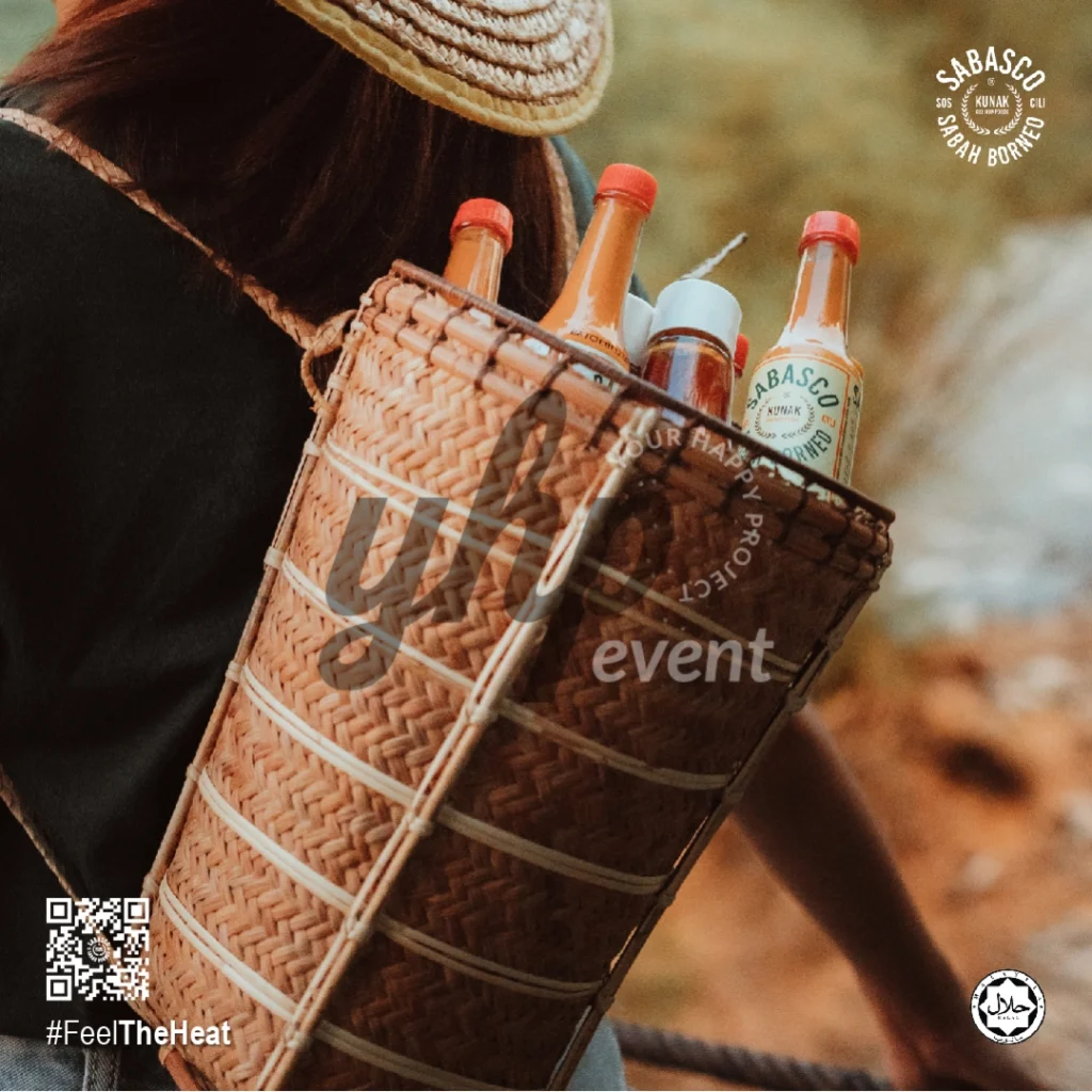 The Local Sabah Chili Sauce Brand That’s Heating Up 9 Woman on a suspension bridge overlooking a river valley with Sabasco Sabah Borneo chili sauce bottles in a woven basket