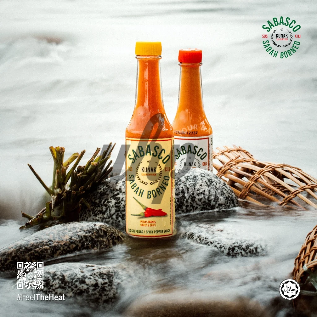 The Local Sabah Chili Sauce Brand That’s Heating Up 10 Two Sabasco Sabah Borneo chili sauce bottles standing on river stones with flowing water and woven baskets nearby
