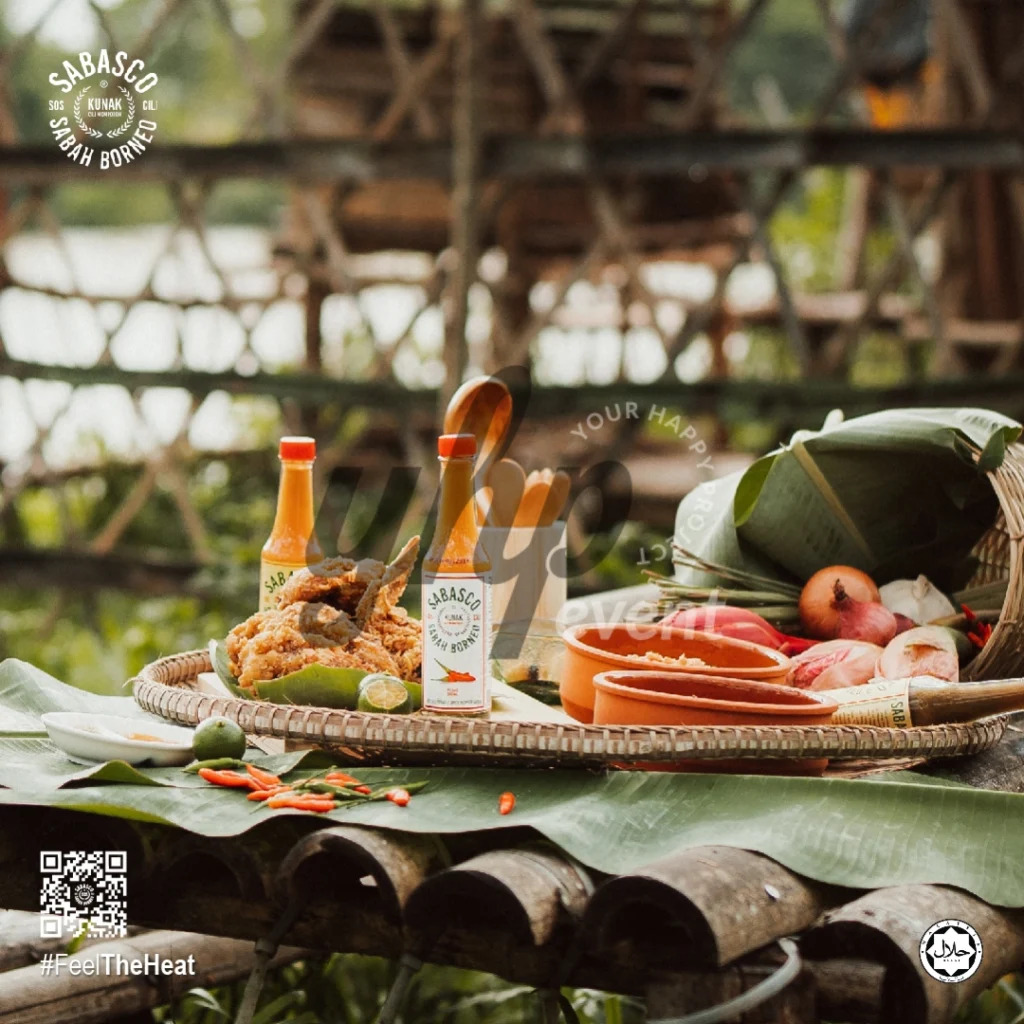 The Local Sabah Chili Sauce Brand That’s Heating Up 12 Rustic outdoor food setup with Sabasco Sabah Borneo chili sauce bottles, fried chicken, limes, onions, and banana leaves