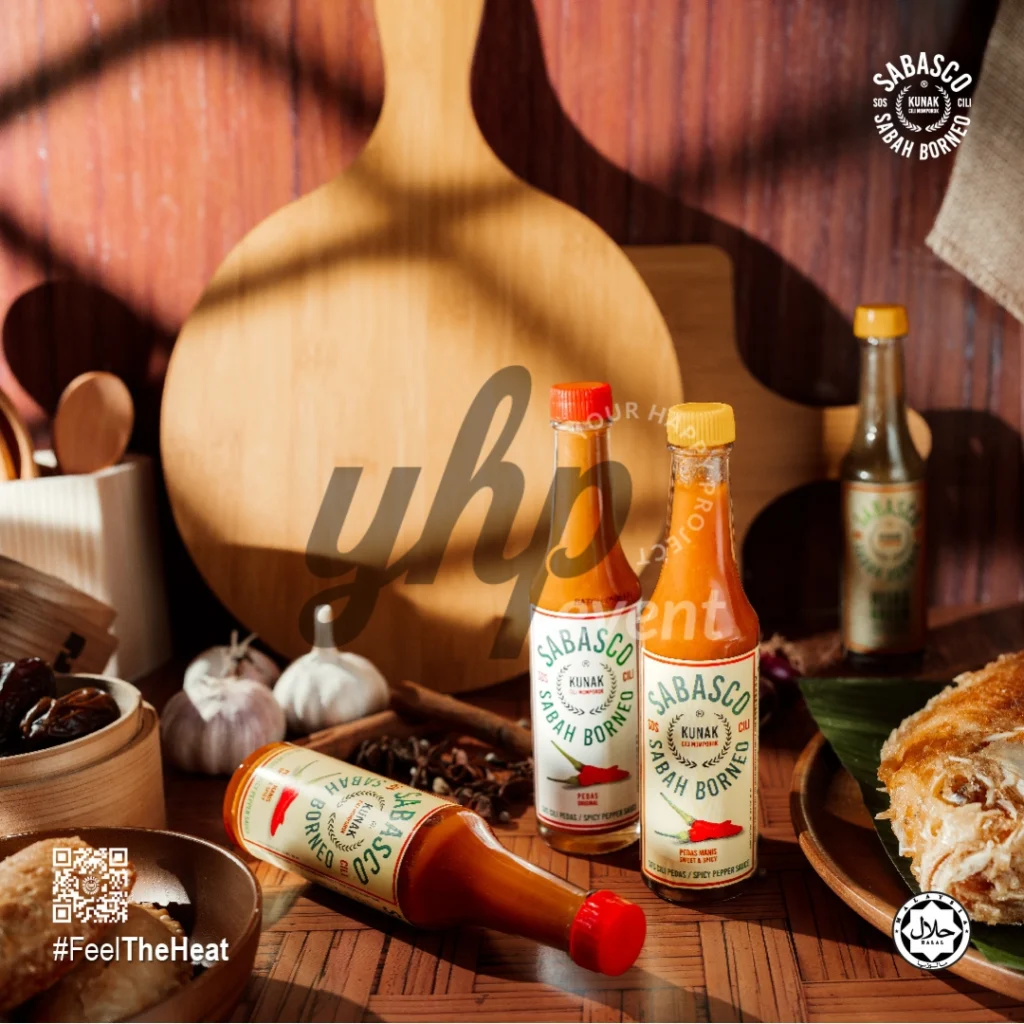 The Local Sabah Chili Sauce Brand That’s Heating Up 5 Sabasco Sabah Borneo chili sauce bottles styled in a rustic kitchen scene with spices, garlic, and wooden boards