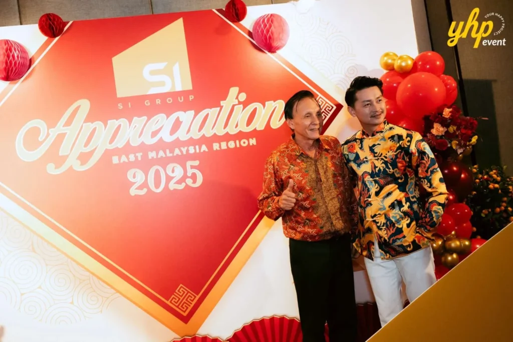 Two men posing at the Smart Infinite Group Appreciation 2025 photo wall wearing traditional batik and festive shirts