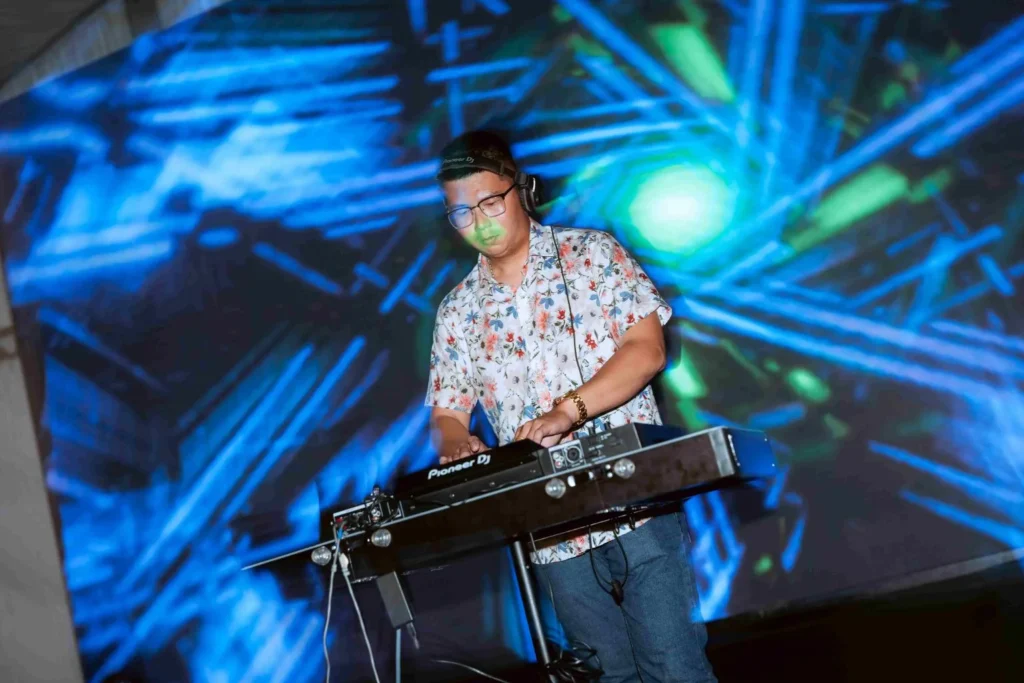 Spark Fest Carnival l Karambunai Hotel 11 DJ wearing headphones performs on stage in front of vivid blue and green digital visuals at a live event
