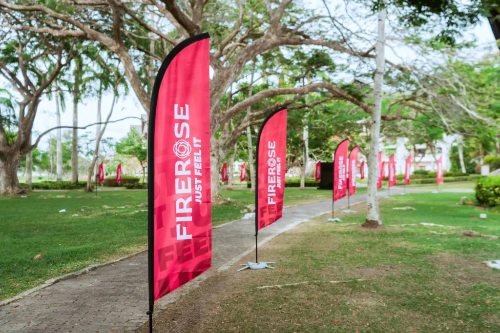 Spark Fest Carnival l Karambunai Hotel 13 Branded red feather flags line a garden walkway entrance path beneath large trees at an outdoor resort