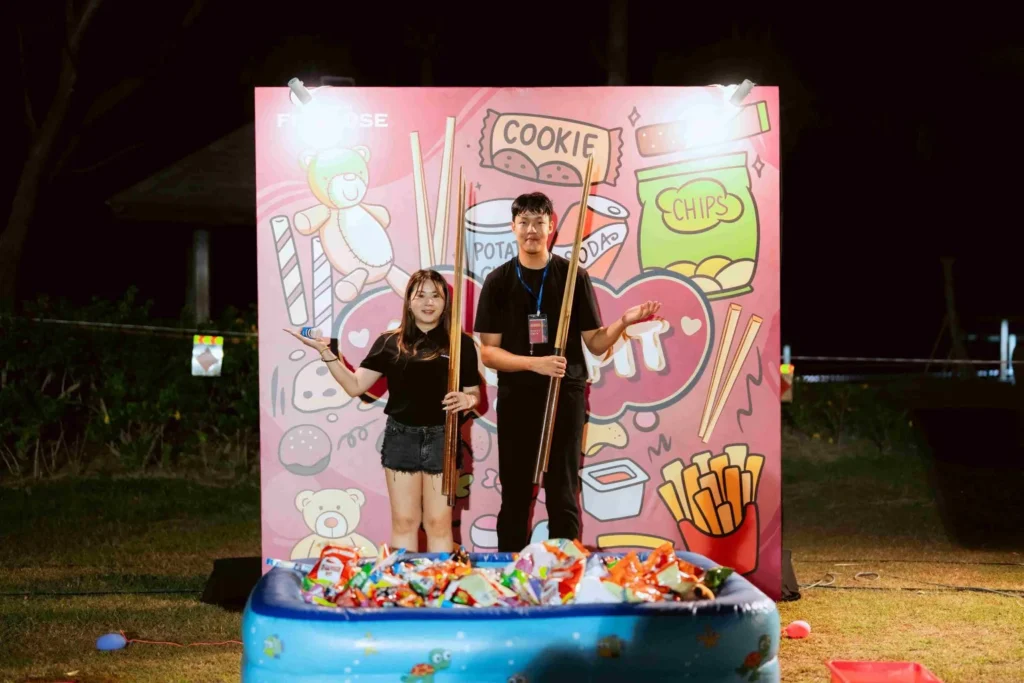 Spark Fest Carnival l Karambunai Hotel 5 Two participants stand with bamboo poles beside a snack pit game booth at an outdoor night carnival activity